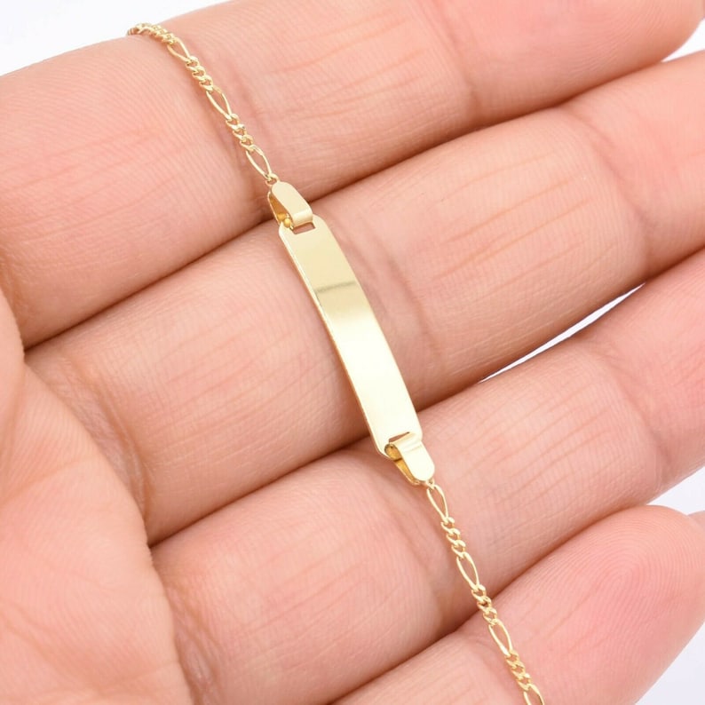 14K solid yellow gold baby ID Figaro chain bracelet held in hand