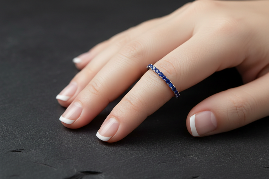 Sapphire eternity band worn on pinky finger against dark slate background
